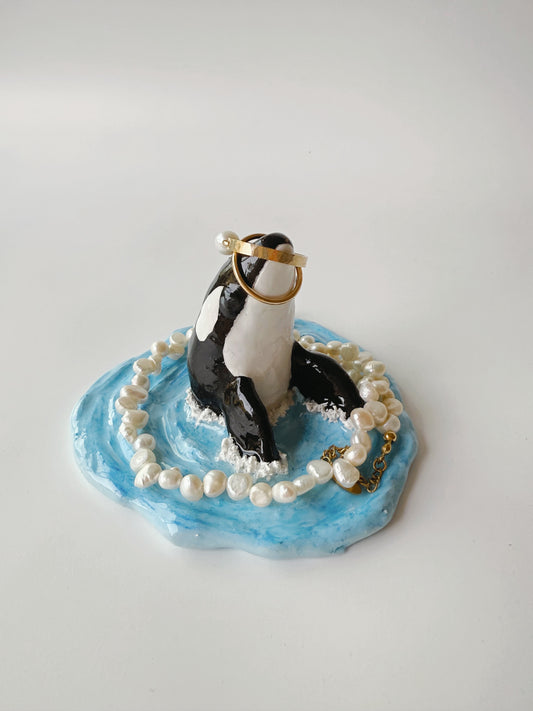 orca figurine with pearls and a ring on a blue base against a white background