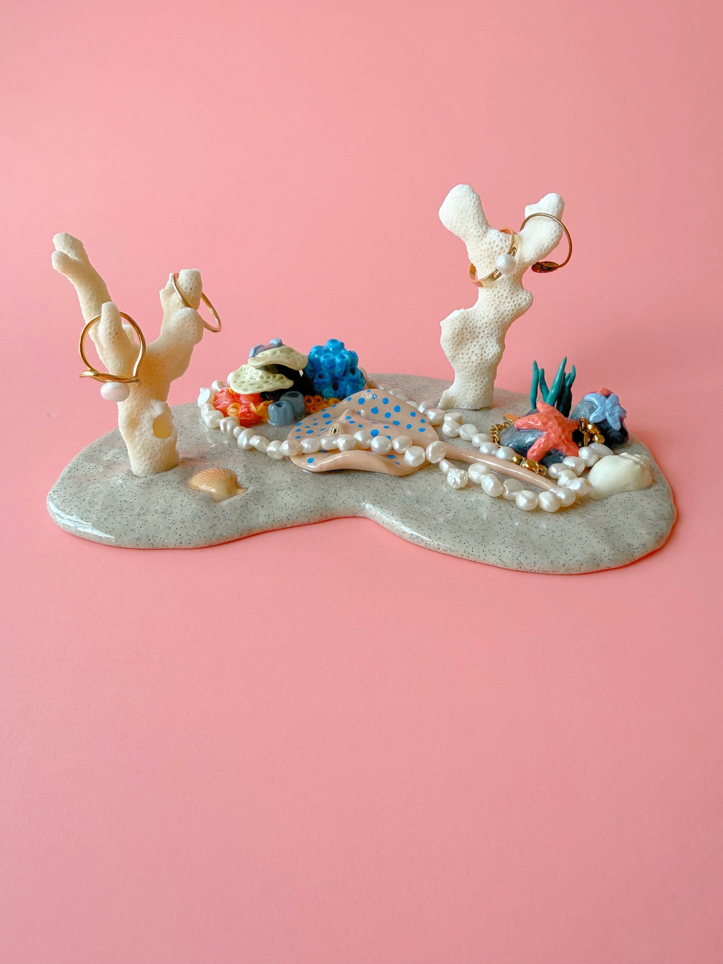 Decorative jewelry display with figurines and jewelry on a pink background