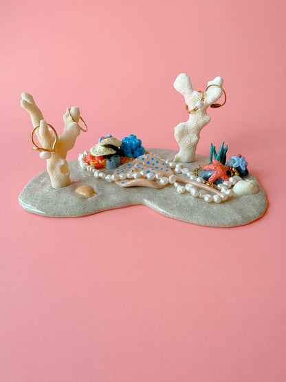 Decorative jewelry display with figurines and jewelry on a pink background