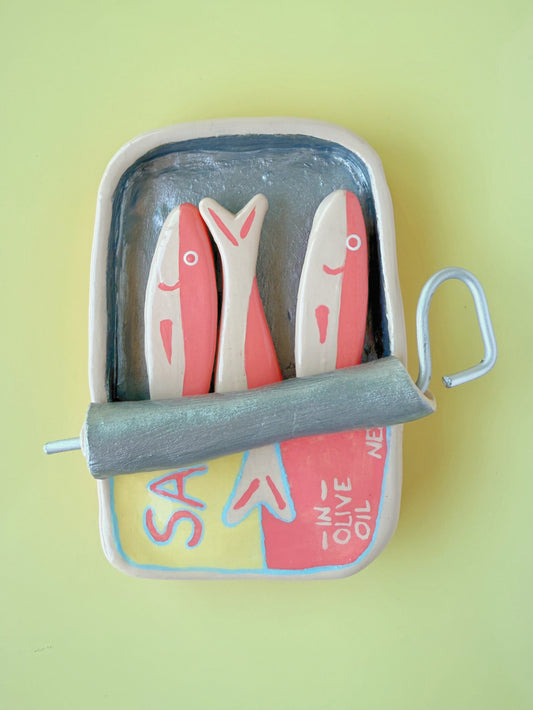 Pink and yellow sardine tin magnet with three pink sardine fish magnets inside the tin on a yellow background 
